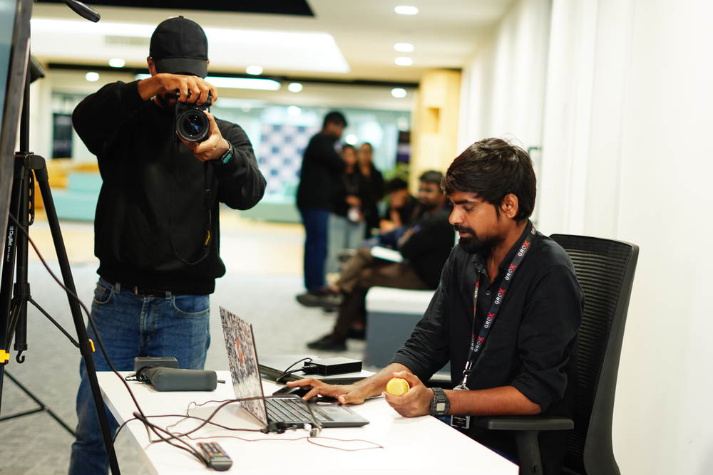 A student editing at a desk while a camera films over his shoulder
